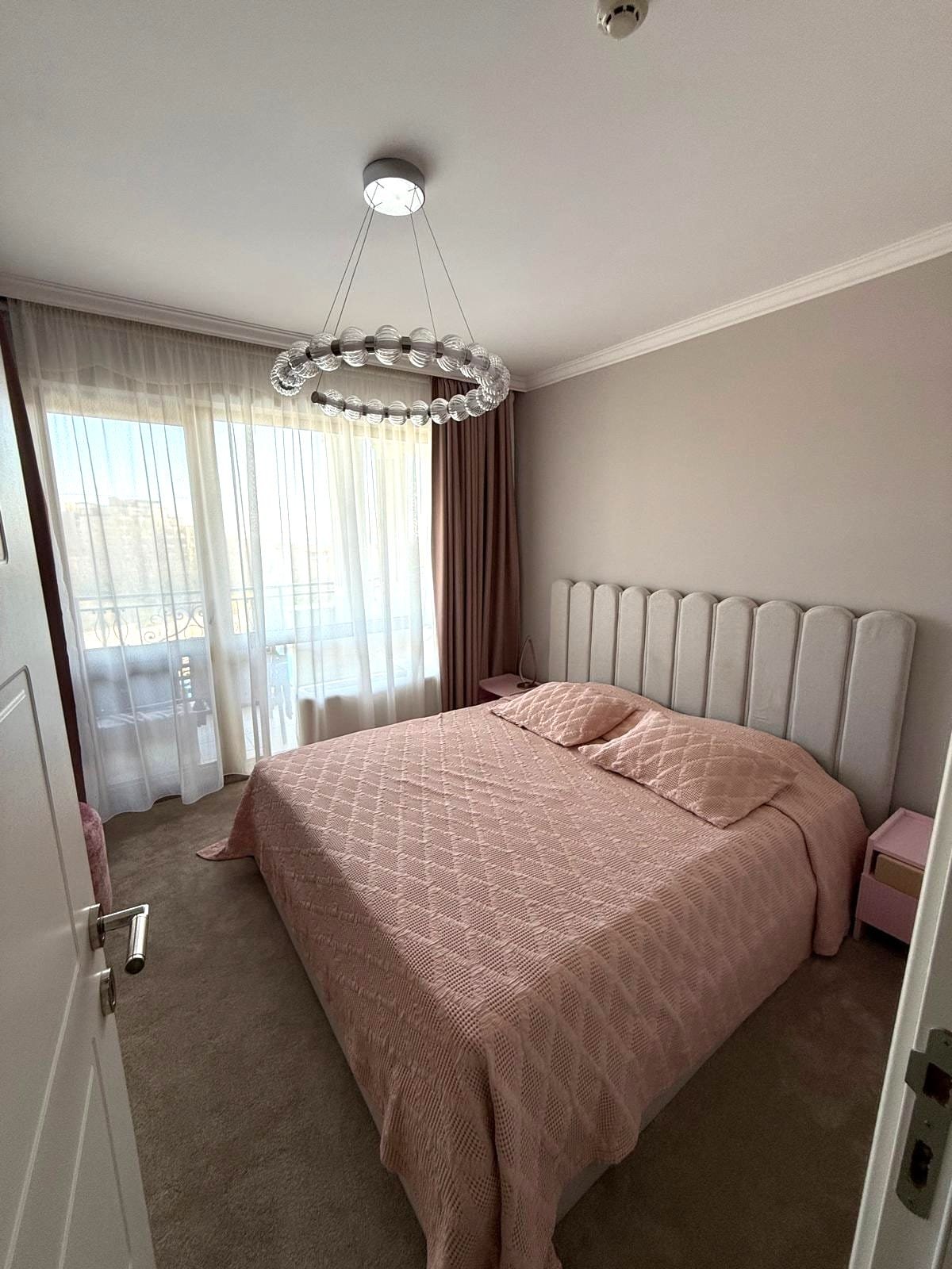 Современная спальня с двуспальной кроватью, мягким светом и стильным дизайном, идеальна для покупки недвижимости в Болгарии.