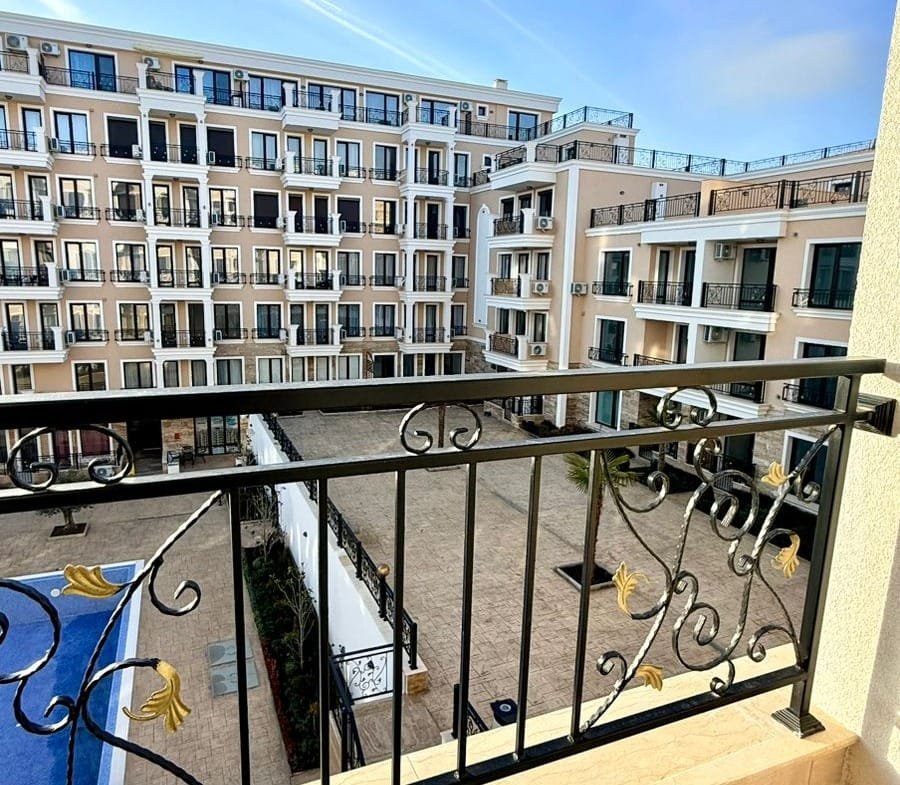 Балкон с кованым ограждением, вид на закрытый двор и бассейн, новые апартаменты для продажи в Болгарии.