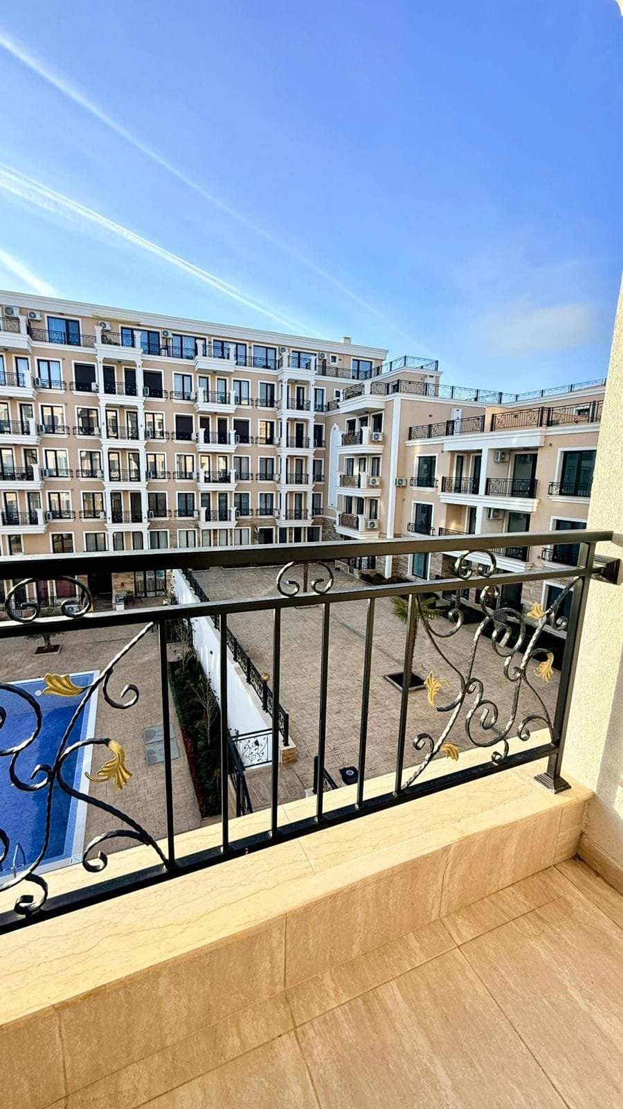 Балкон с кованым ограждением, вид на закрытый двор и бассейн, новые апартаменты для продажи в Болгарии.