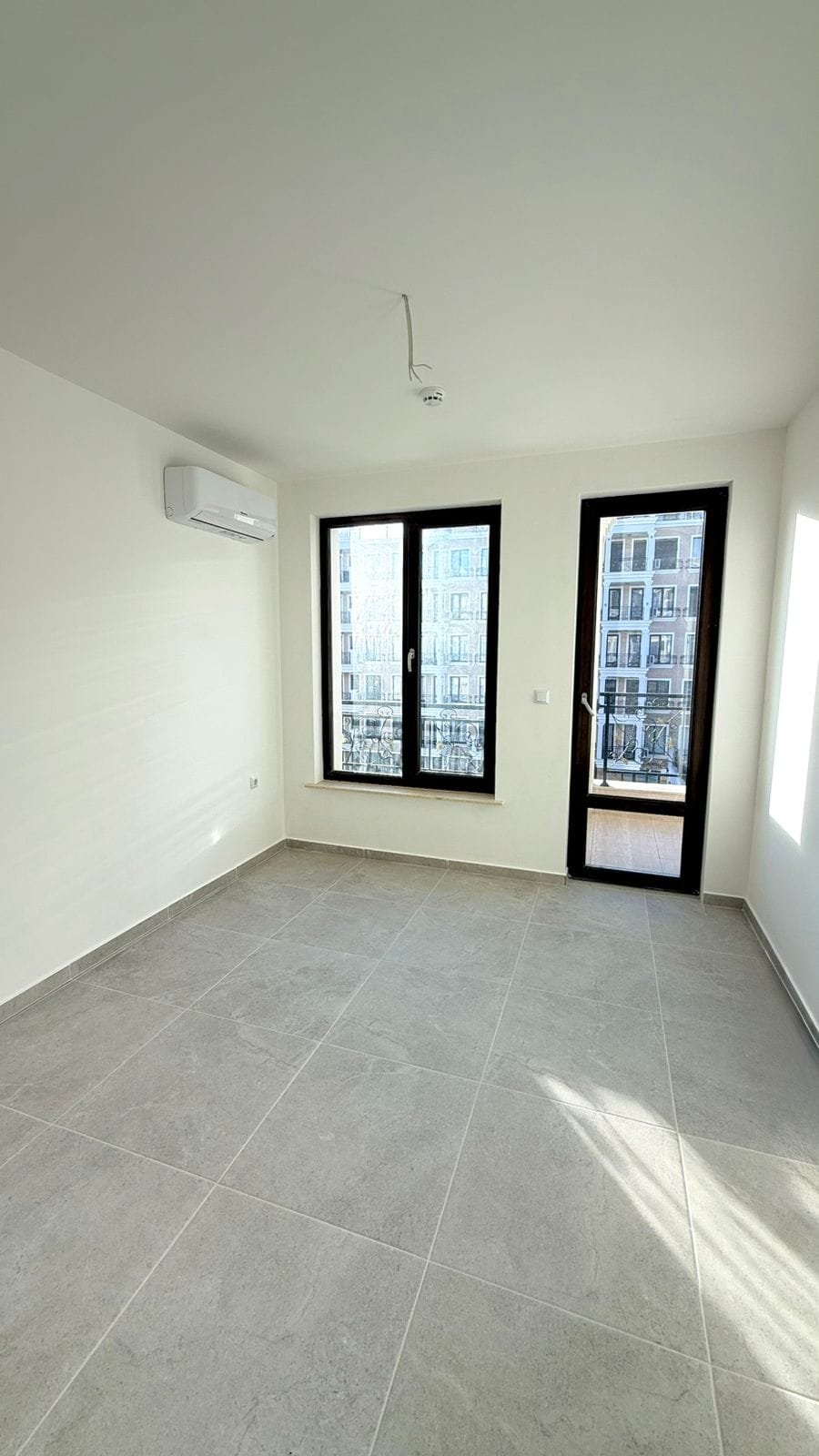 Пустая квартира с большими окнами, светлым интерьером и плиточным полом, готовая для продажи в Болгарии.