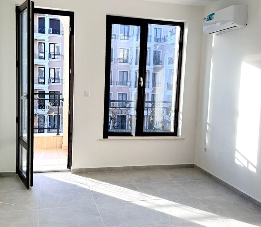 Современная квартира в Болгарии с большими окнами, светлыми стенами и плиточным полом, готовая к продаже.