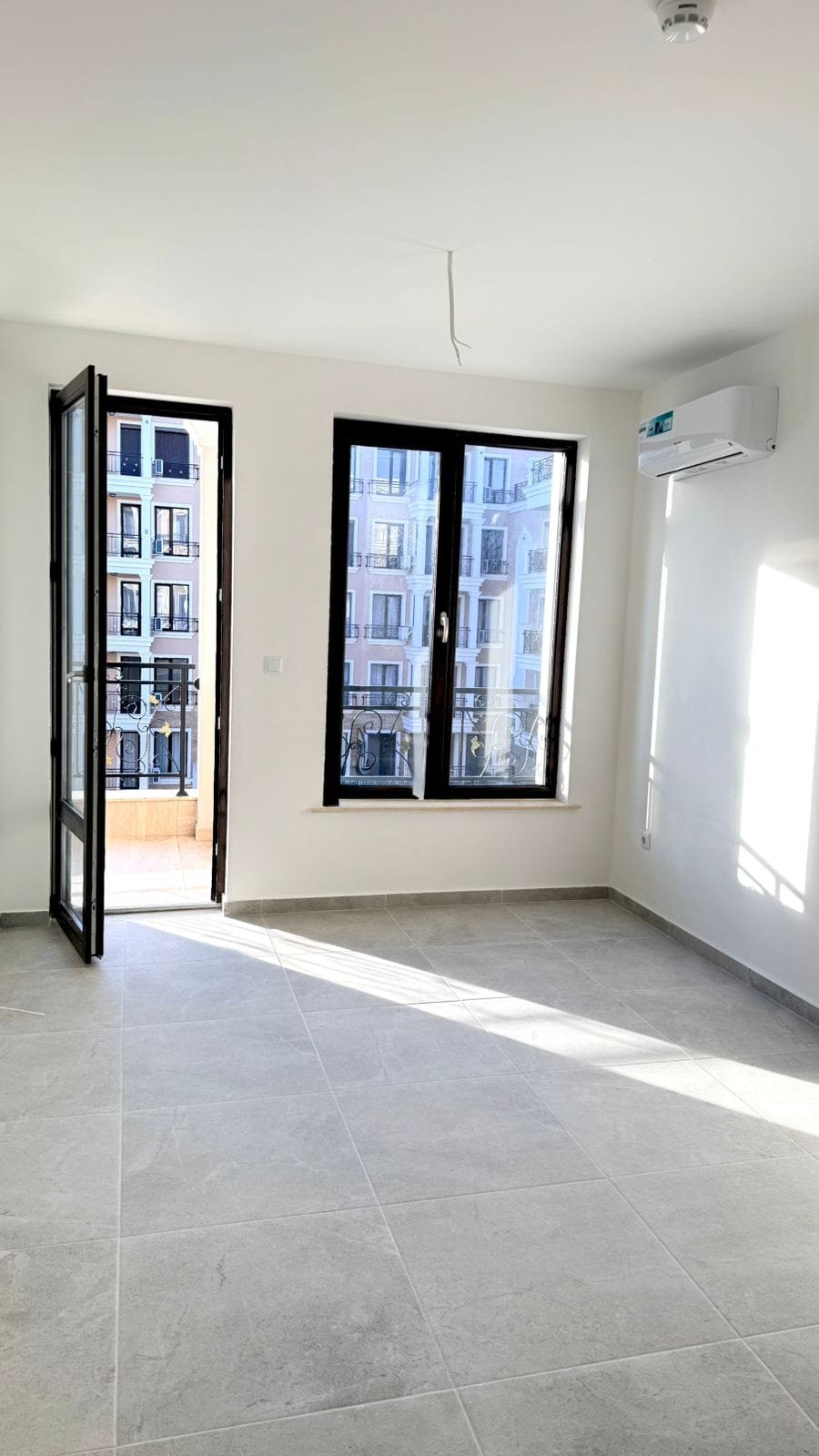 Современная квартира в Болгарии с большими окнами, светлыми стенами и плиточным полом, готовая к продаже.