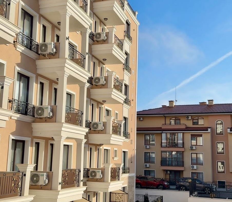 Многоэтажный жилой комплекс с балконами, кондиционерами и ухоженной территорией, идеальный для покупки недвижимости в Болгарии.