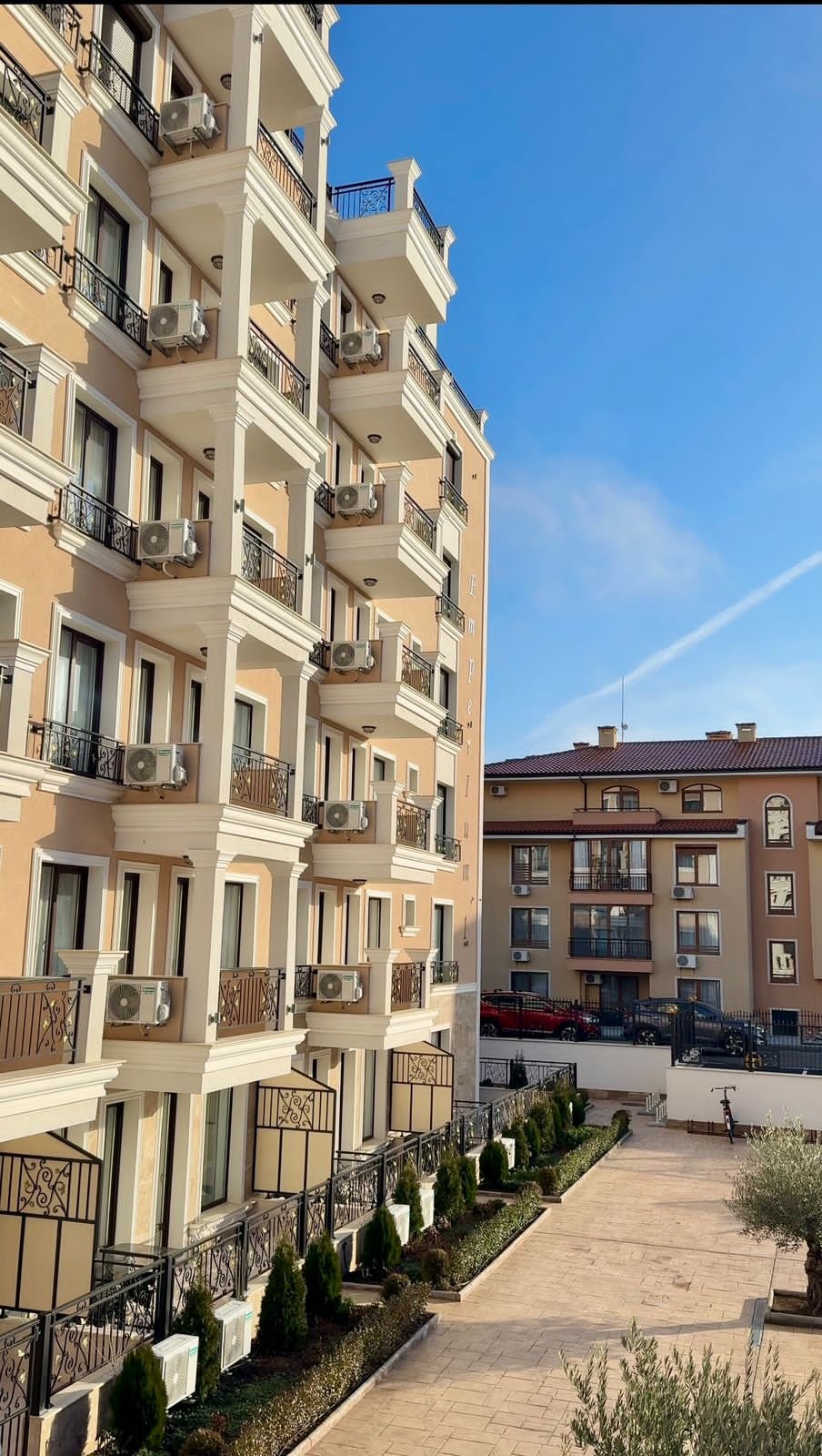 Многоэтажный жилой комплекс с балконами, кондиционерами и ухоженной территорией, идеальный для покупки недвижимости в Болгарии.