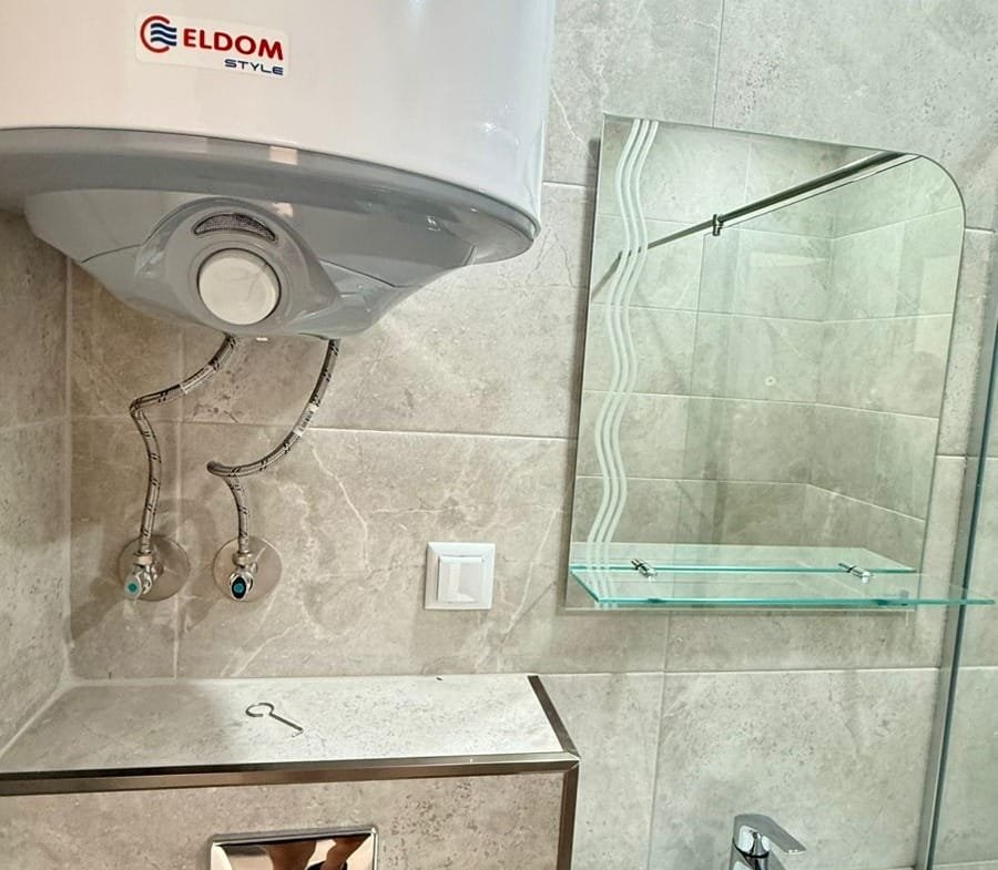 Современная ванная комната с бойлером, раковиной и зеркалом, подходящая для покупки недвижимости в Болгарии.