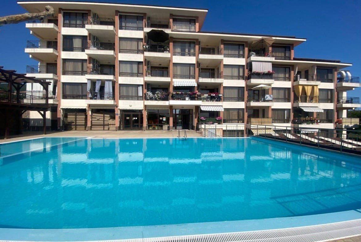 Современный жилой комплекс с балконами и бассейном на фоне ясного голубого неба, идеален для покупки недвижимости в Болгарии.