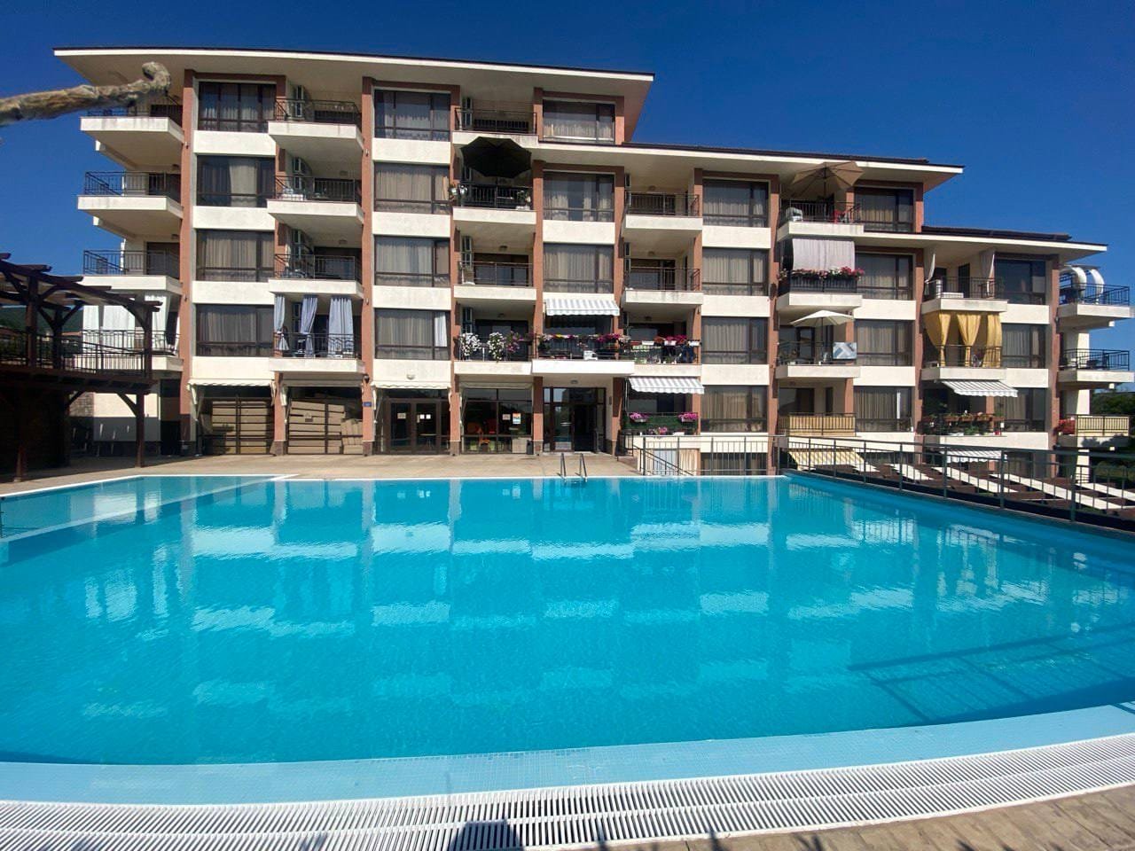 Современный жилой комплекс с балконами и бассейном на фоне ясного голубого неба, идеален для покупки недвижимости в Болгарии.