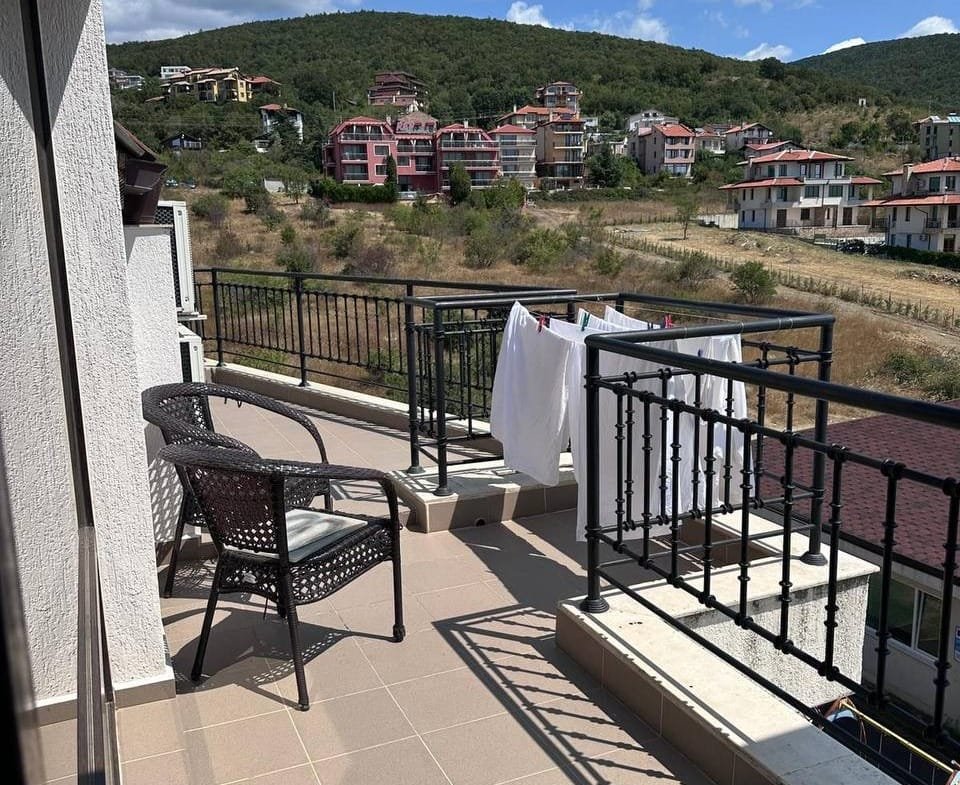 Балкон с плетёной мебелью, развешенное бельё и вид на окружающие дома в курортной зоне Болгарии.