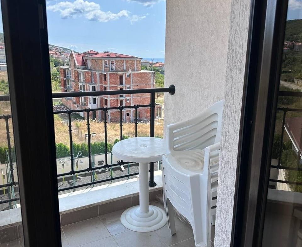 Балкон с пластиковыми стульями и столом, вид на строящиеся здания, голубое небо, купля-продажа недвижимости в Болгарии.