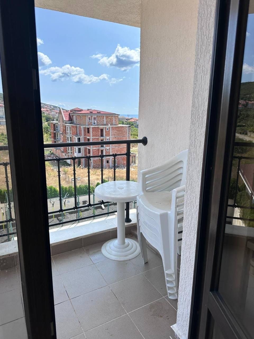 Балкон с пластиковыми стульями и столом, вид на строящиеся здания, голубое небо, купля-продажа недвижимости в Болгарии.