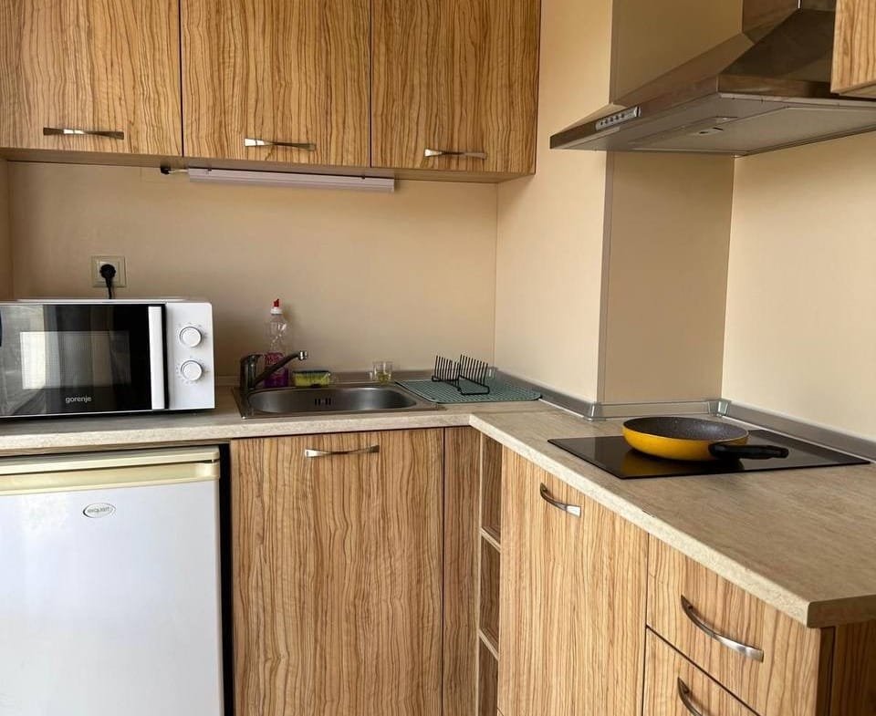 Современная кухня с деревянными фасадами, микроволновой печью, плитой и мойкой, подходящая для покупки недвижимости в Болгарии.