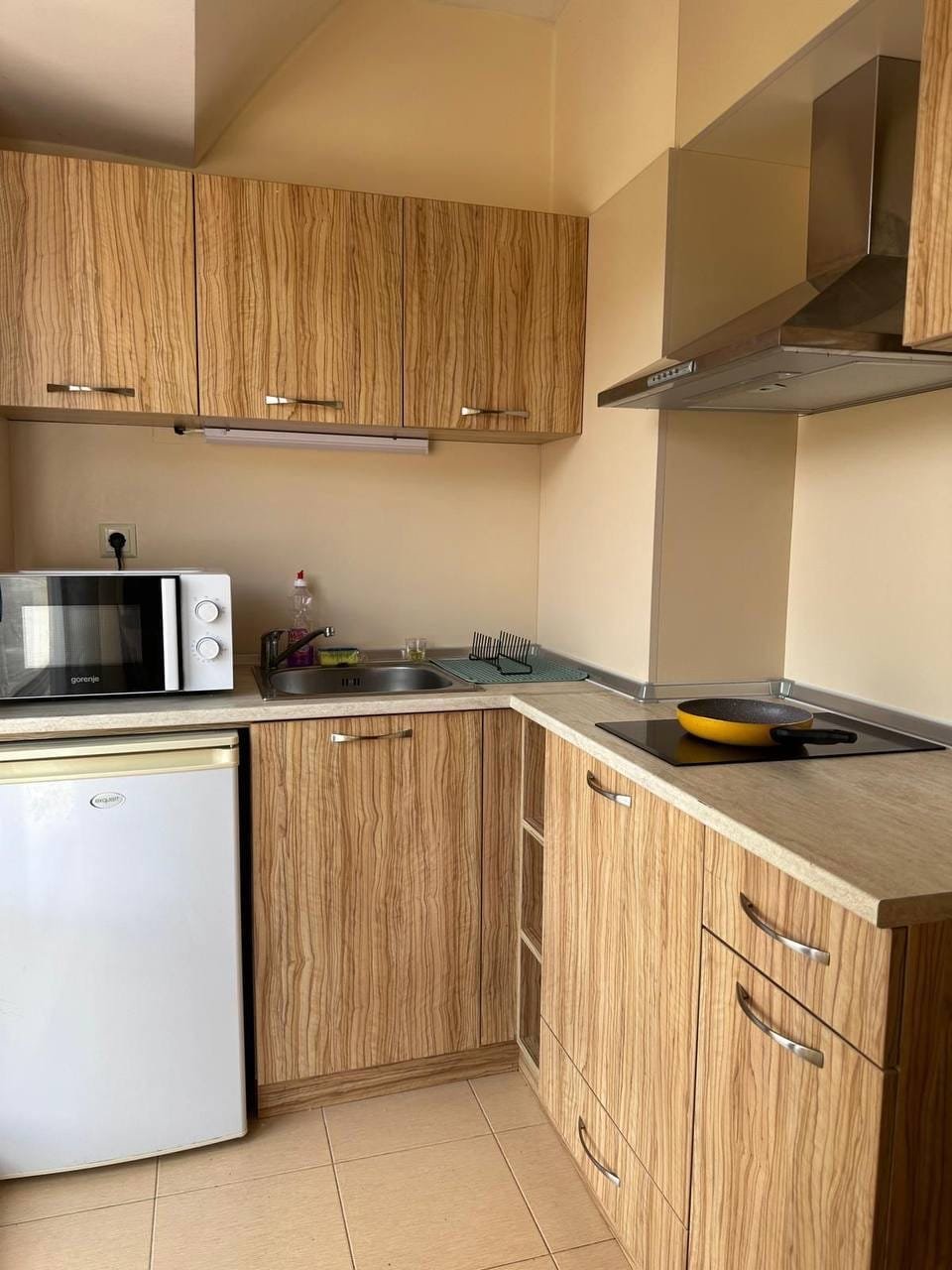 Современная кухня с деревянными фасадами, микроволновой печью, плитой и мойкой, подходящая для покупки недвижимости в Болгарии.