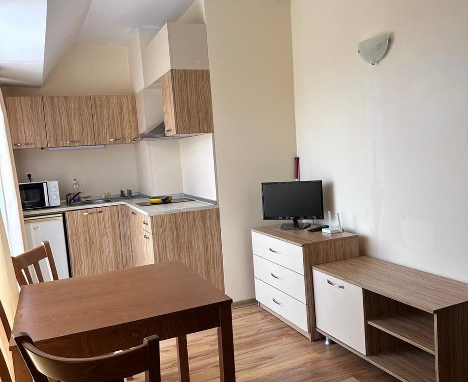 Современная квартира в Болгарии с кухней, столом и телевизором, оформленная в светлых тонах и деревянных элементах.