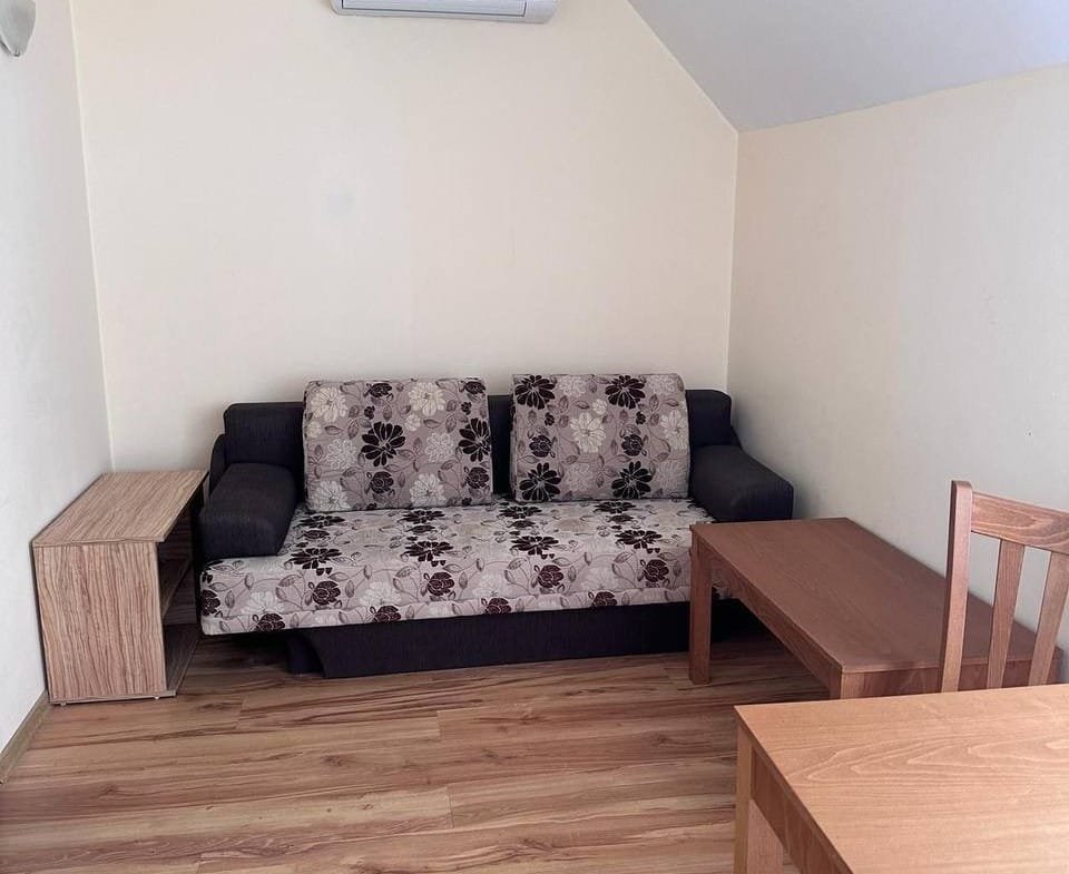 Современная и уютная комната с диваном, деревянным столом и стульями, идеальная для покупки недвижимости в Болгарии.