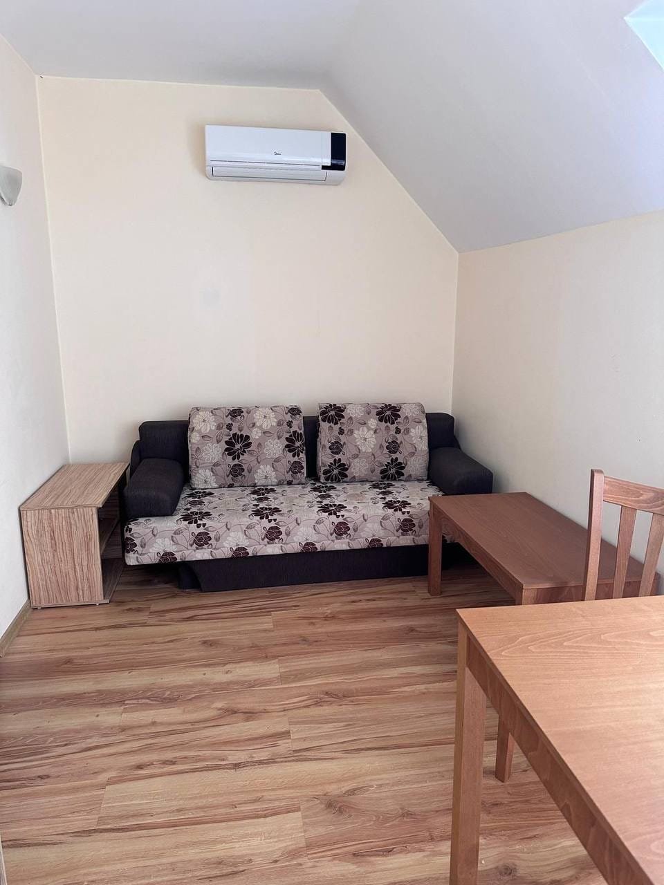 Современная и уютная комната с диваном, деревянным столом и стульями, идеальная для покупки недвижимости в Болгарии.