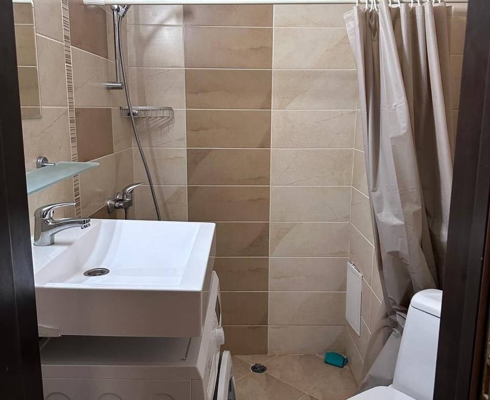 Современная ванная комната в Болгарии с душевой кабиной, стиральной машиной и унитазом, оформленная в нейтральных тонах.