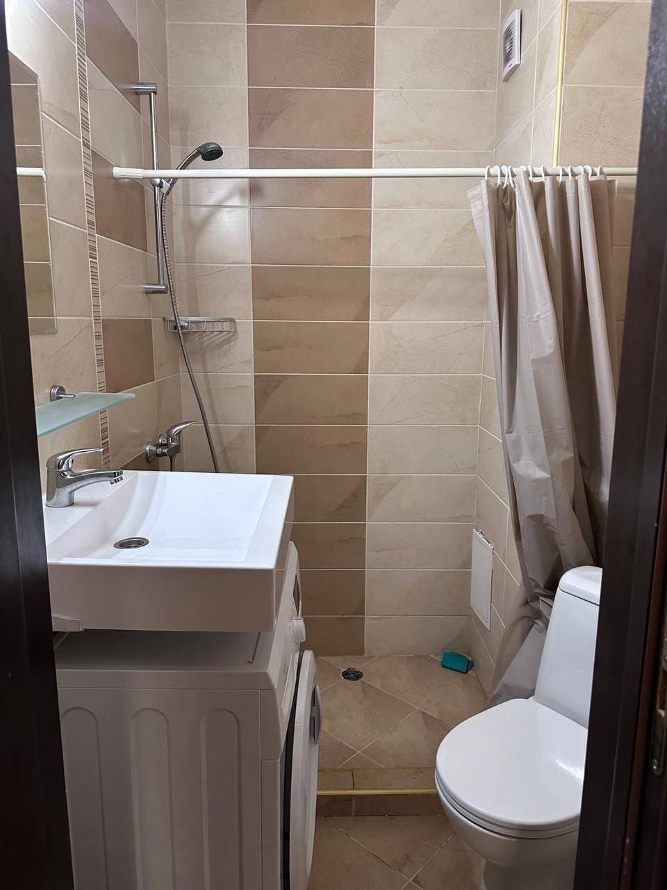 Современная ванная комната в Болгарии с душевой кабиной, стиральной машиной и унитазом, оформленная в нейтральных тонах.