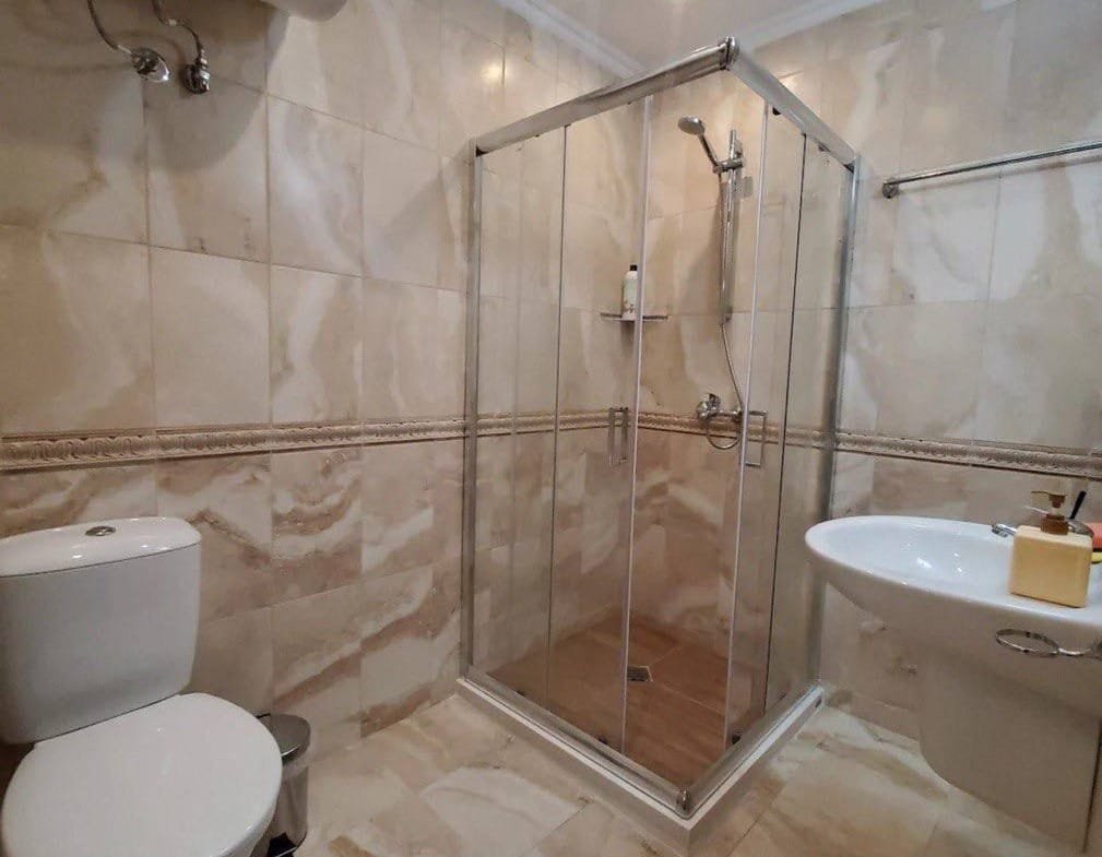 Современная ванная комната с душевой кабиной, унитазом и раковиной, оформленная в бежевых тонах для комфортного проживания.