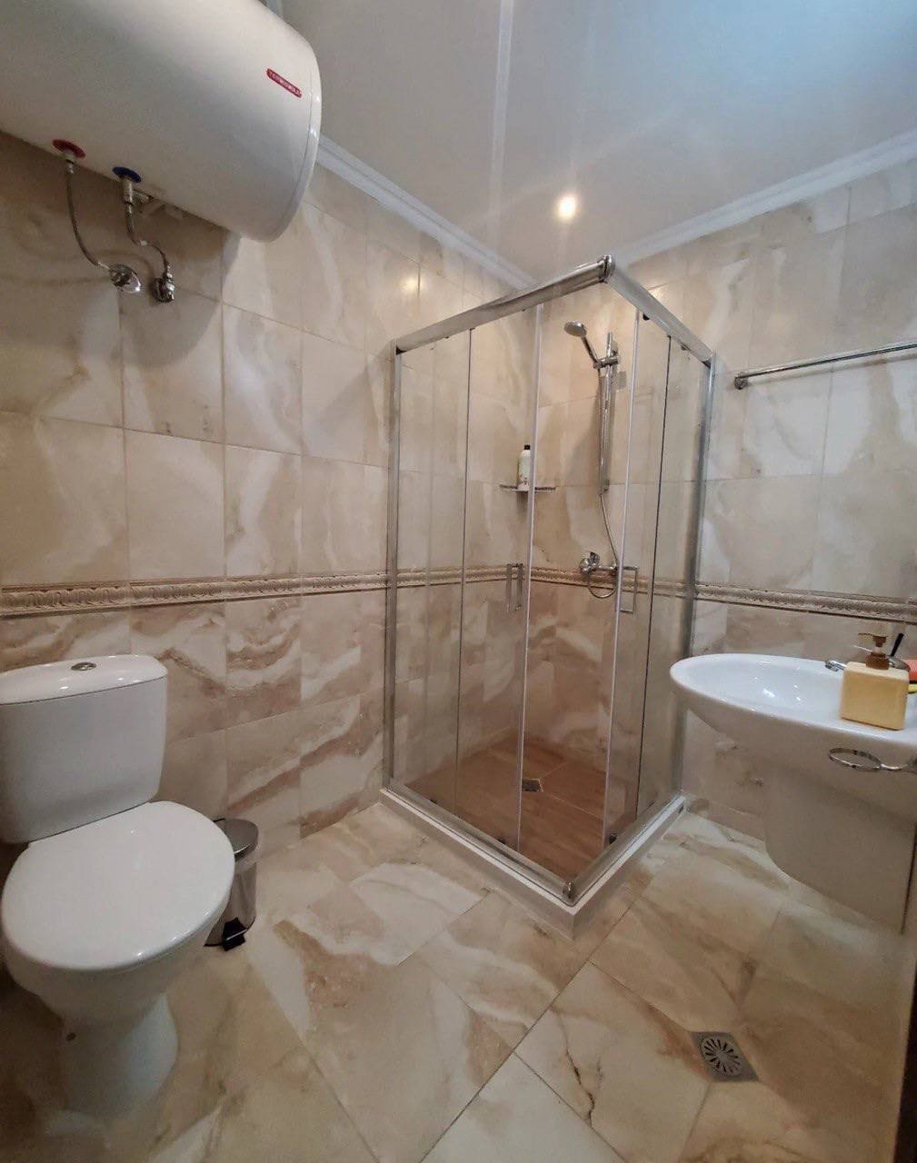 Современная ванная комната с душевой кабиной, унитазом и раковиной, оформленная в бежевых тонах для комфортного проживания.