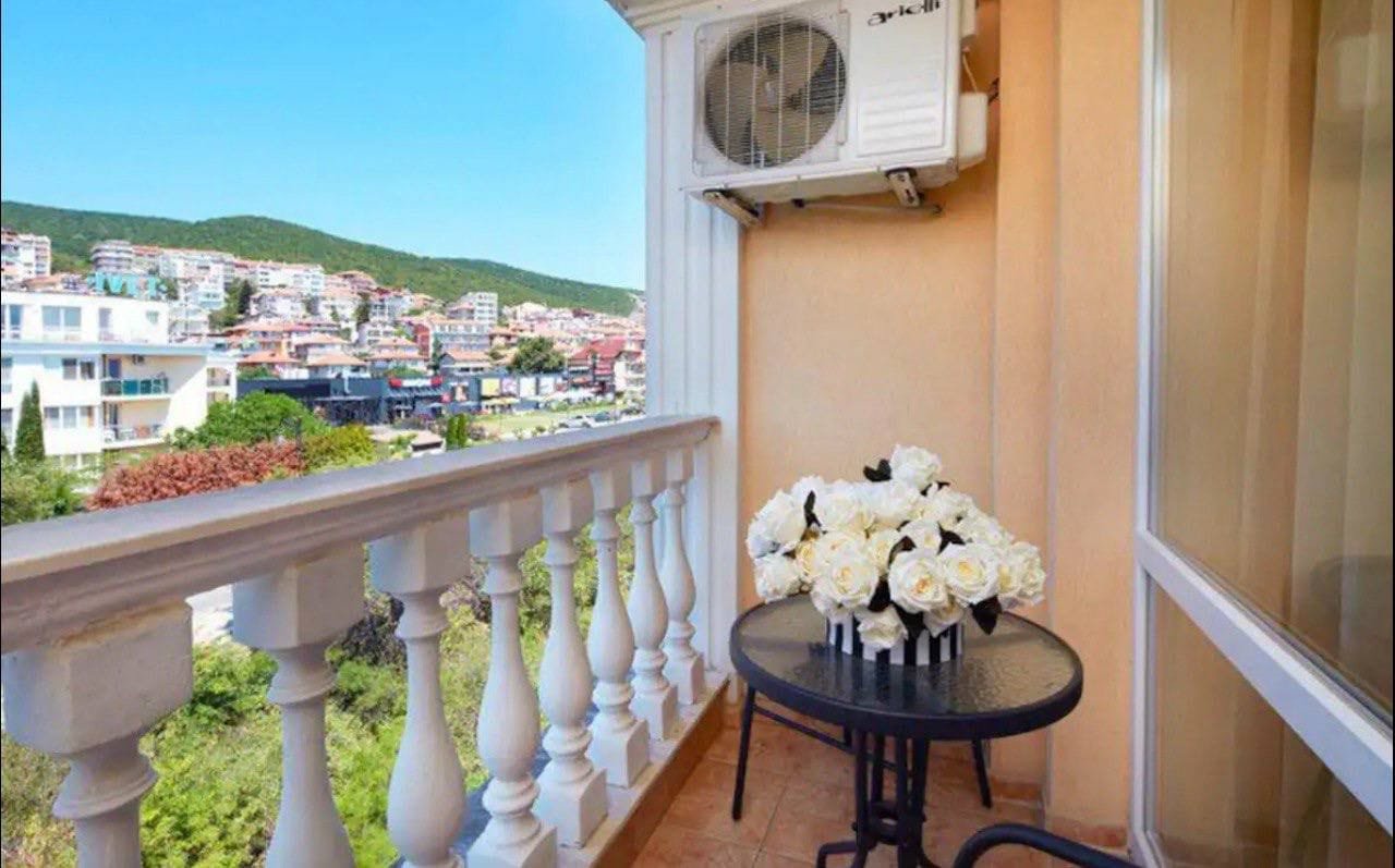 Балкон с черным столом и вазой белых роз, виды на жилье и горы, акцент на продаже недвижимости в Болгарии.