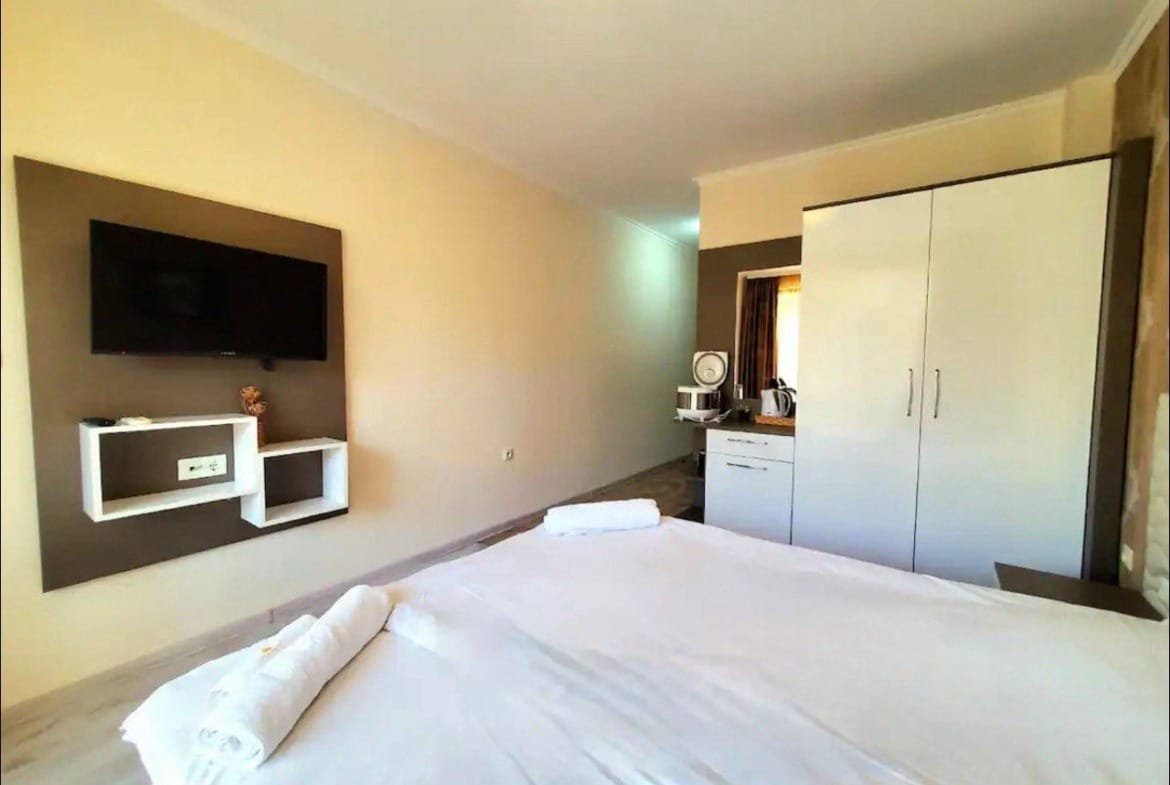 Современная комната с большой кроватью, телевизором, шкафом и мини-кухней, подходящая для аренды в Болгарии.