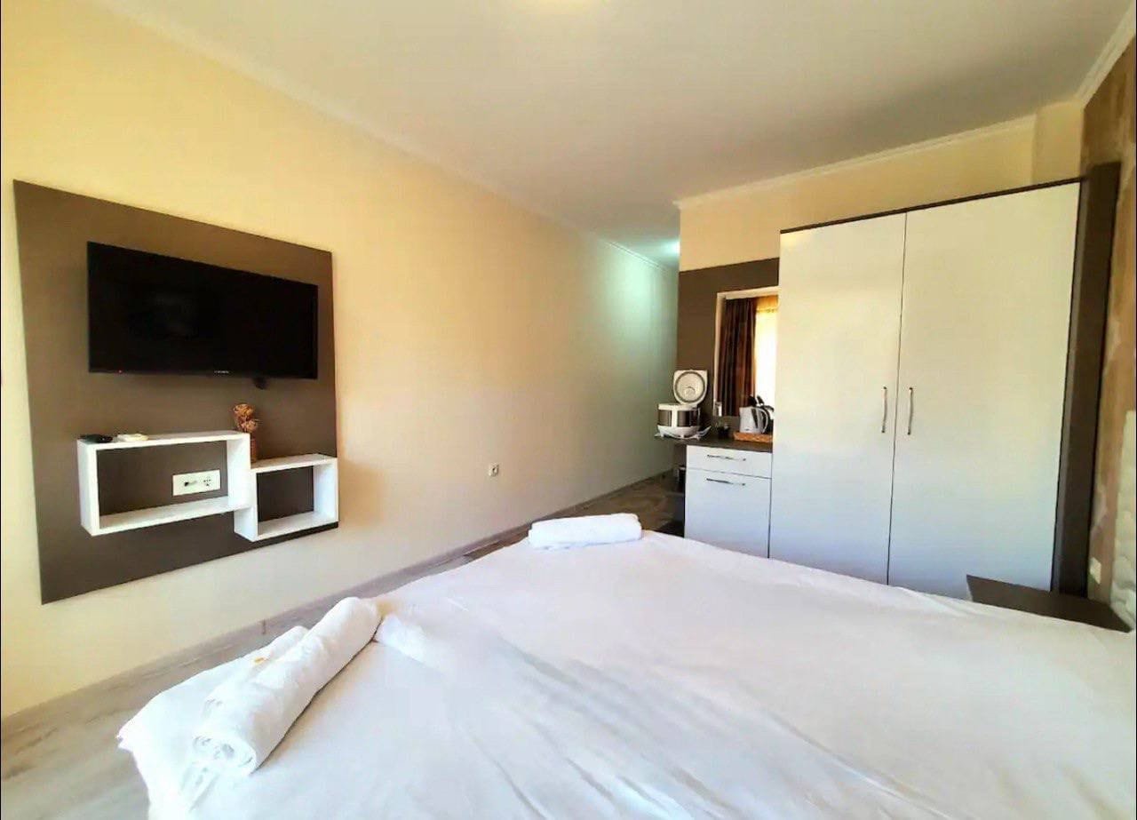 Современная комната с большой кроватью, телевизором, шкафом и мини-кухней, подходящая для аренды в Болгарии.