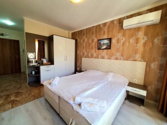 Современная спальня с двуспальной кроватью, шкафом, прикроватными тумбочками и кондиционером в квартире в Болгарии.