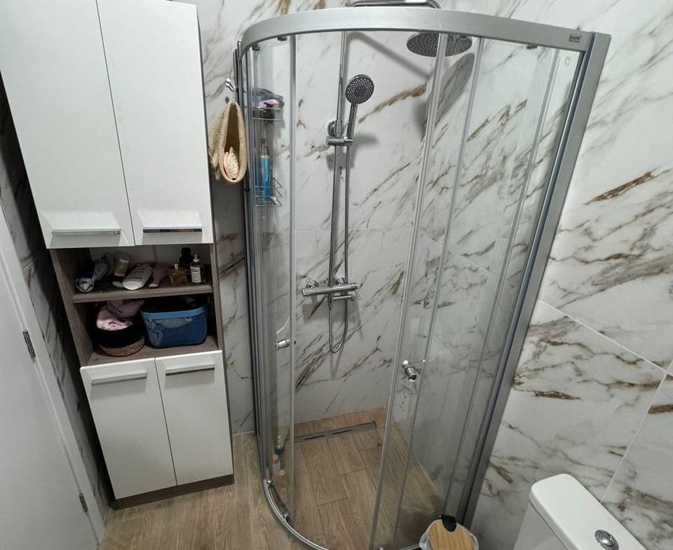 Современная ванная комната с душевой кабиной, сантехникой и стильным шкафом для хранения. Идеально для покупки недвижимости в Болгарии.