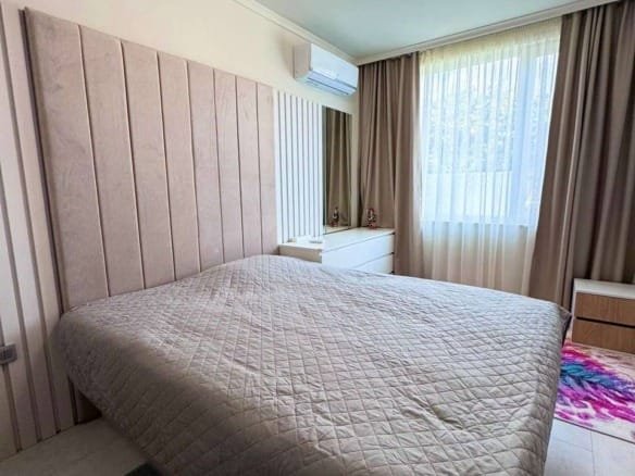 Современная спальня с большой кроватью, светлыми шторами и комфортной атмосферой, идеальная для отдыха в Болгарии.