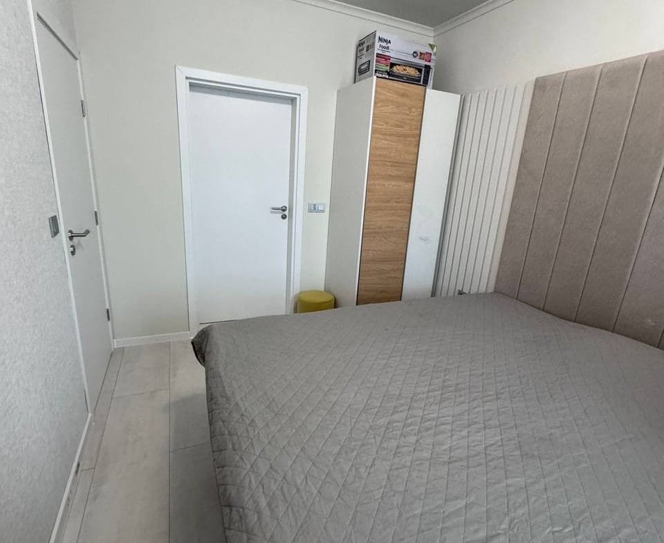 Современная спальня в квартире в Болгарии с двуспальной кроватью и встроенным шкафом на светлом фоне.