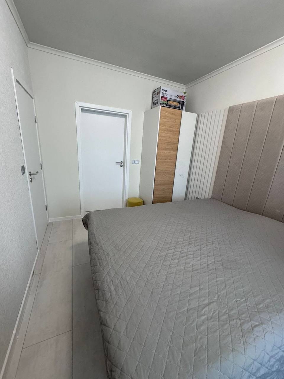 Современная спальня в квартире в Болгарии с двуспальной кроватью и встроенным шкафом на светлом фоне.