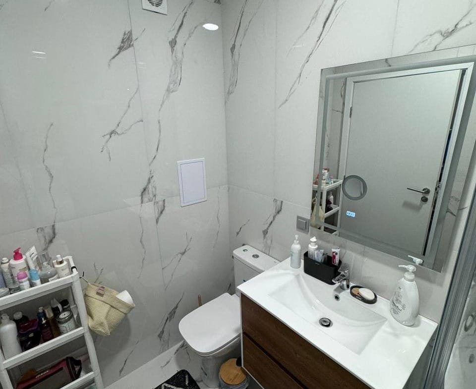 Современный санузел с белой плиткой, деревянным шкафчиком и зеркалом, идеально подходит для дома в Болгарии.