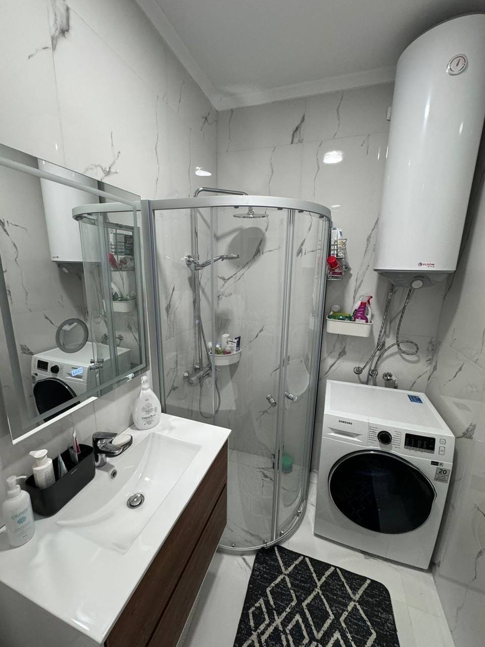 Современная ванная комната с душевой кабиной, стиральной машиной и зеркалом, оформленная в нейтральных тонах.