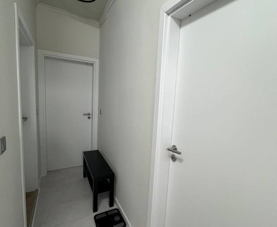 Современный коридор с белыми стенами, дверями и черной табуреткой, демонстрирующий спокойный интерьер для покупки недвижимости в Болгарии.