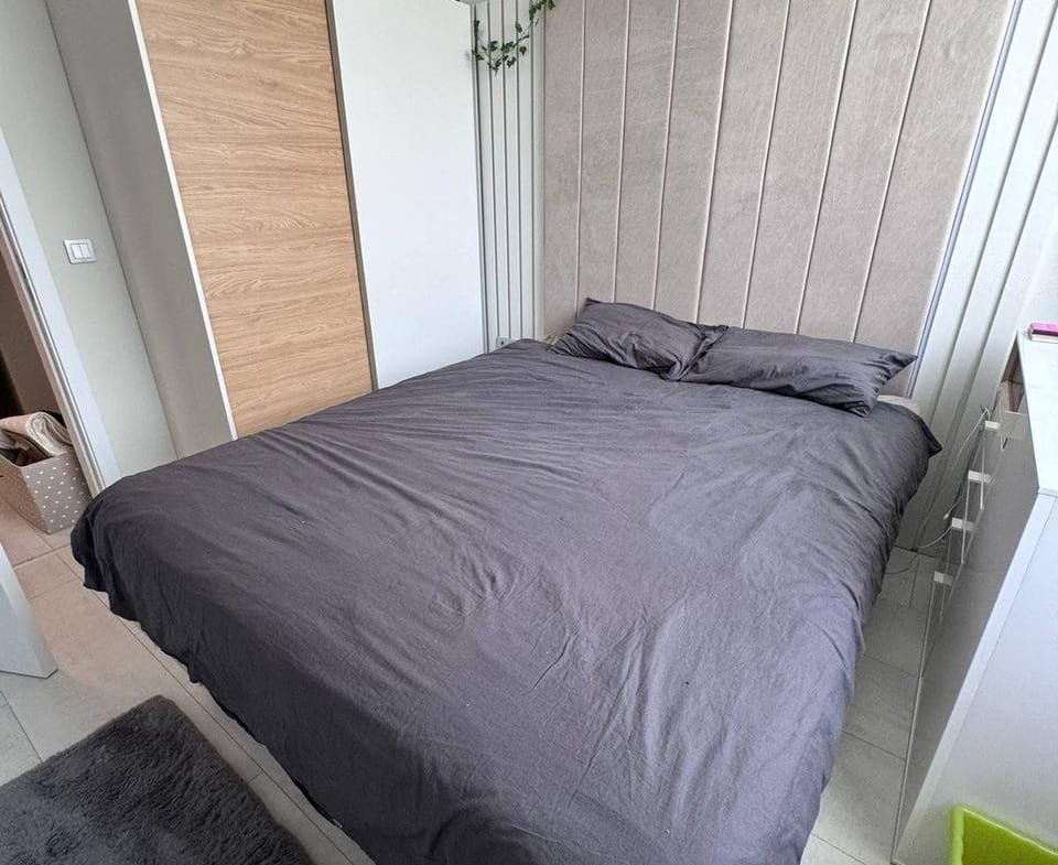 Современная спальня с двуспальной кроватью, светлыми стенами и минималистичной мебелью в Болгарии. уютная атмосфера.