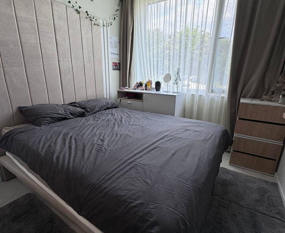 Современная спальня с серым постельным бельем, большой окном и минималистичной мебелью, идеальная для комфортного проживания в Болгарии.