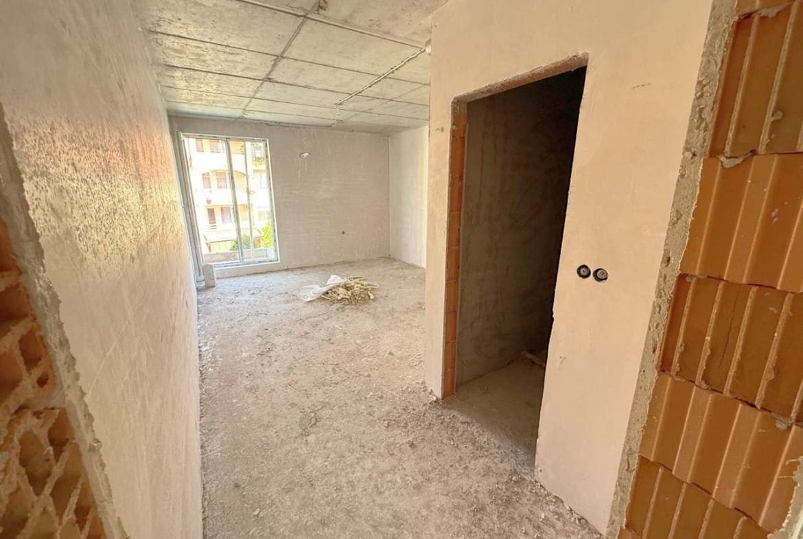 Пустая квартира в Болгарии с белыми стенами и открытой планировкой, готовая для продажи и последующей отделки.