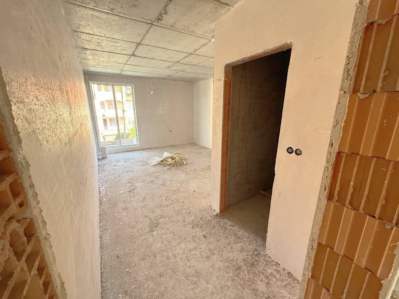 Ремонт квартиры: незавершенное жилое пространство без отделки Пустая квартира в Болгарии с белыми стенами и открытой планировкой, готовая для продажи и последующей отделки.