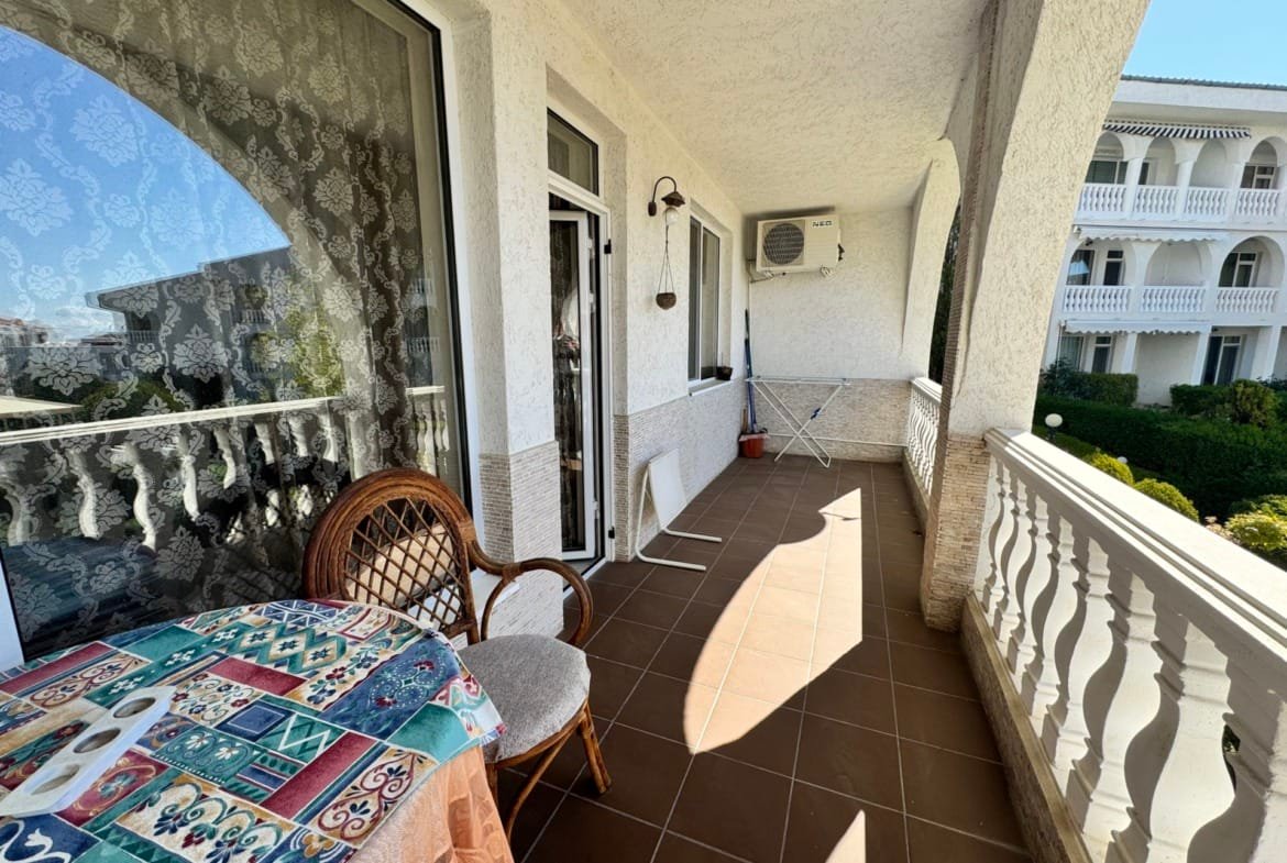 Широкая веранда с плетёной мебелью, столом и сушилкой, окружённая зелеными насаждениями в Болгарии.