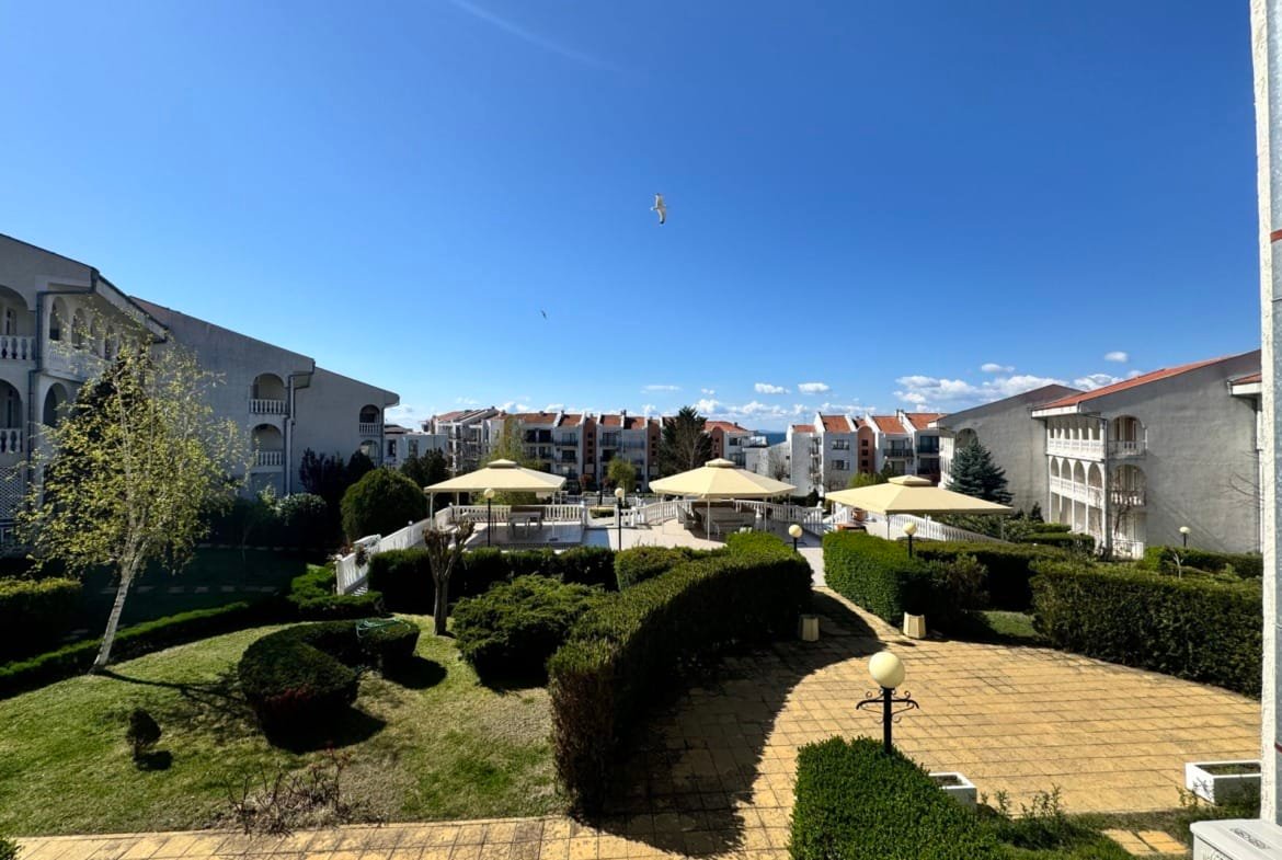 Жилой комплекс в Болгарии с зеленой территорией, зонтиками и чистым небом, подходящий для покупки недвижимости.