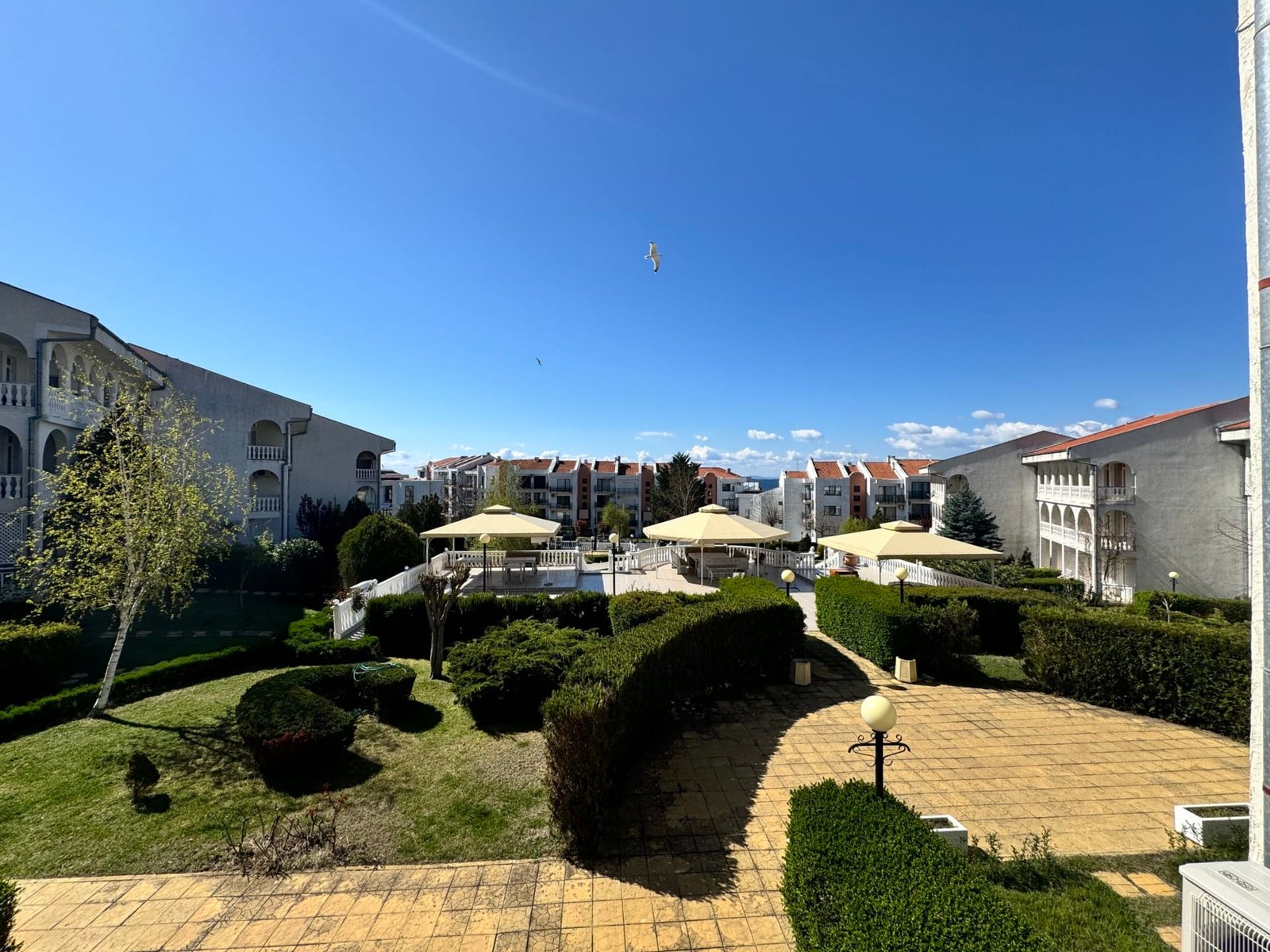 Жилой комплекс в Болгарии с зеленой территорией, зонтиками и чистым небом, подходящий для покупки недвижимости.