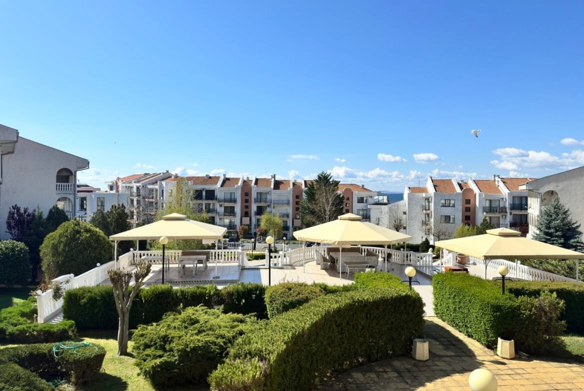 Элегантный комплекс недвижимости в Болгарии с зелеными газонами и зонтиками для отдыха на фоне ясного неба.