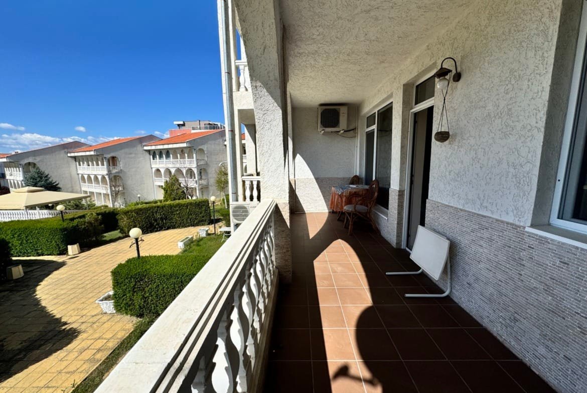 Балкон с видом на ухоженный сад и дома в стиле средиземноморской архитектуры, идеальное место для отдыха в Болгарии.