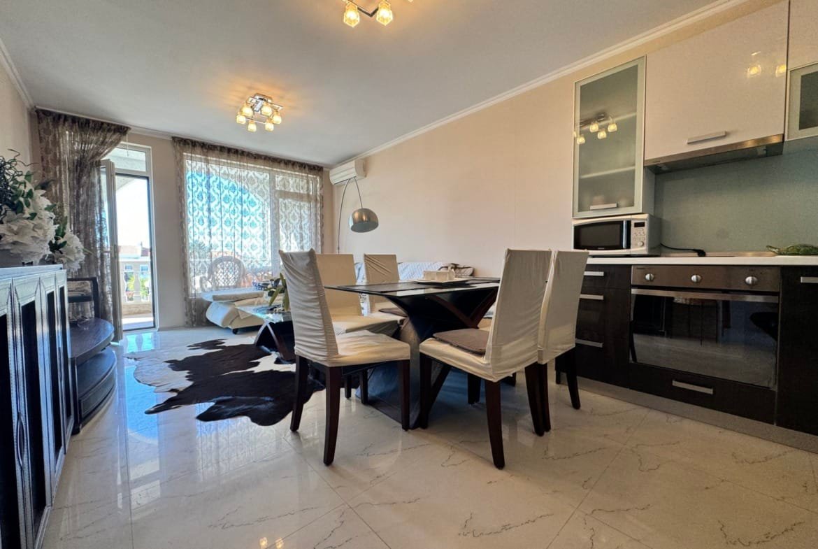 Современный интерьер квартиры в Болгарии с просторной гостиной, столовой зоной и кухонной техникой. Светлые тона, мебель из дерева.