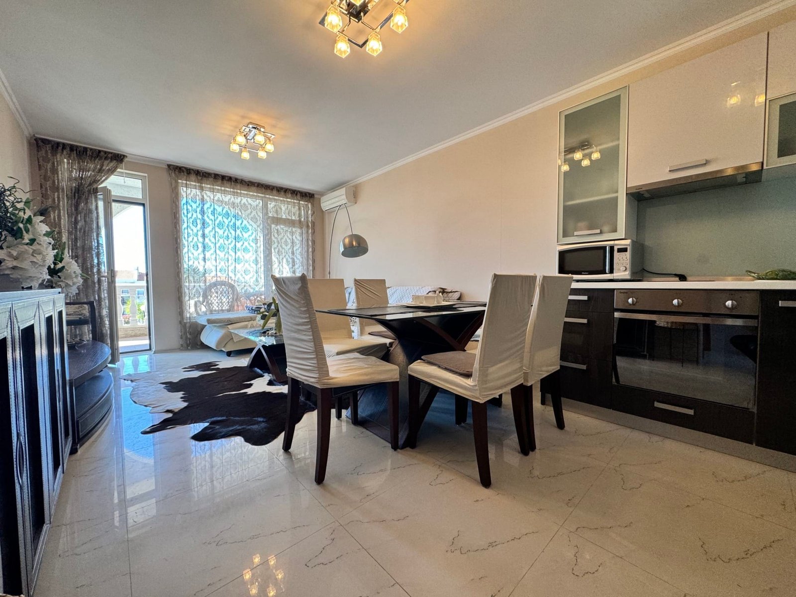 Современный интерьер квартиры в Болгарии с просторной гостиной, столовой зоной и кухонной техникой. Светлые тона, мебель из дерева.