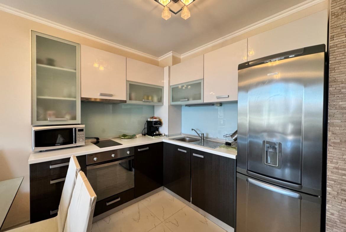 Современная кухня с черно-белыми шкафчиками, металлическим холодильником и техникой, идеальна для покупки недвижимости в Болгарии.