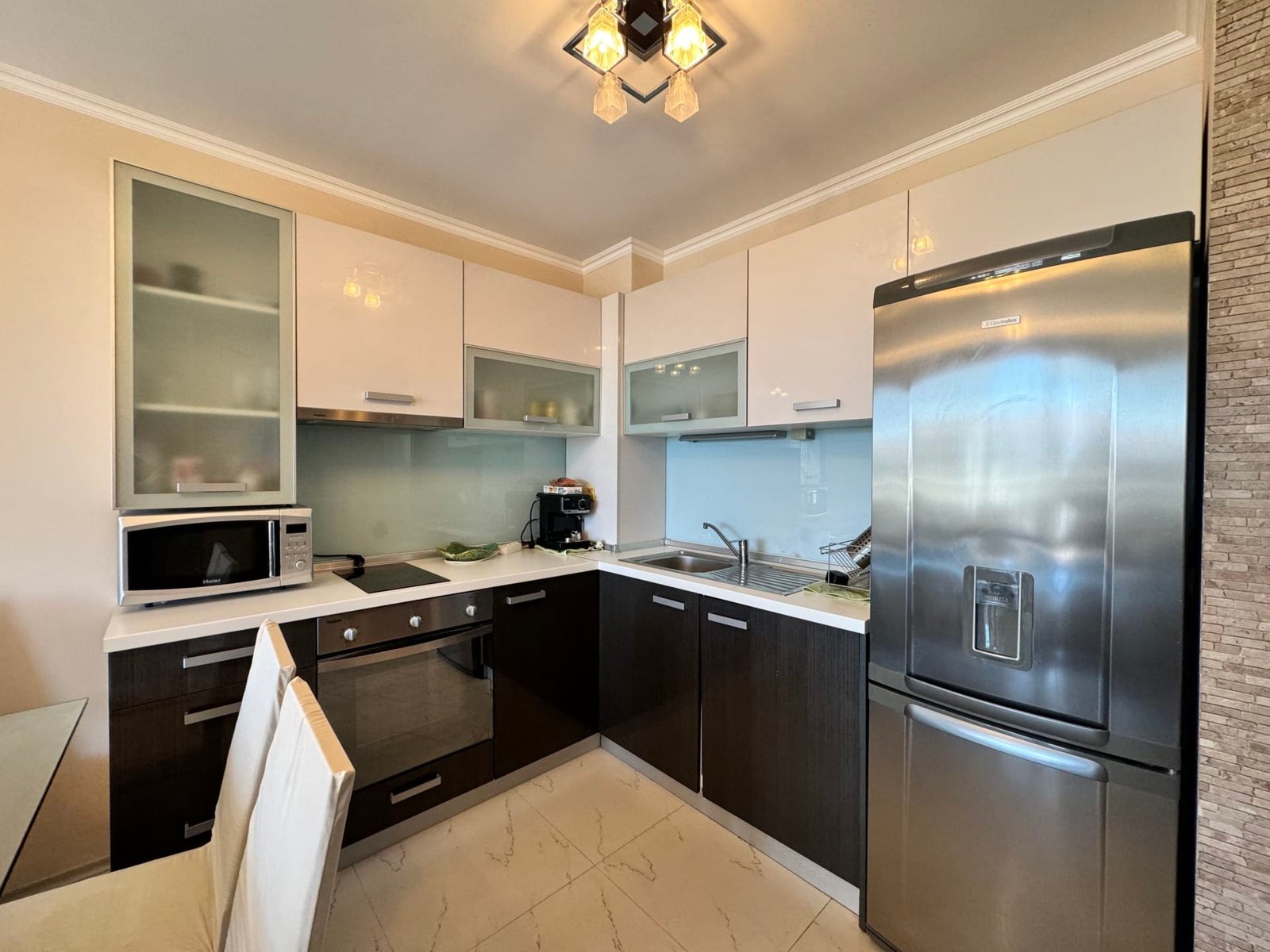 Современная кухня с черно-белыми шкафчиками, металлическим холодильником и техникой, идеальна для покупки недвижимости в Болгарии.