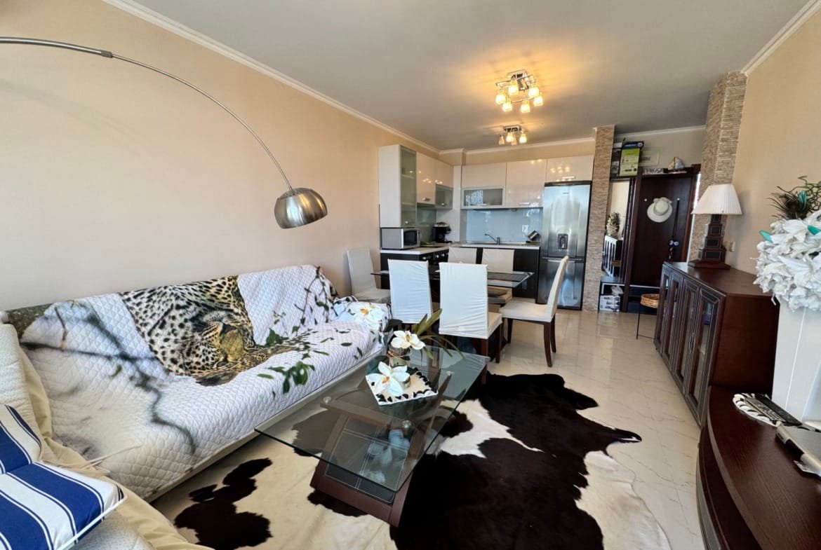 Современный интерьер квартиры в Болгарии с уютной гостиной, стеклянным столом и кухней в открытом формате.