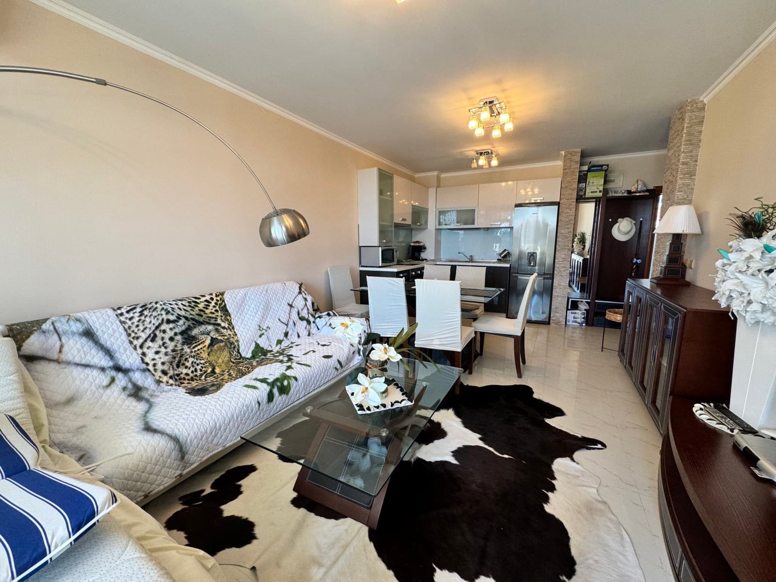 Современный интерьер квартиры в Болгарии с уютной гостиной, стеклянным столом и кухней в открытом формате.