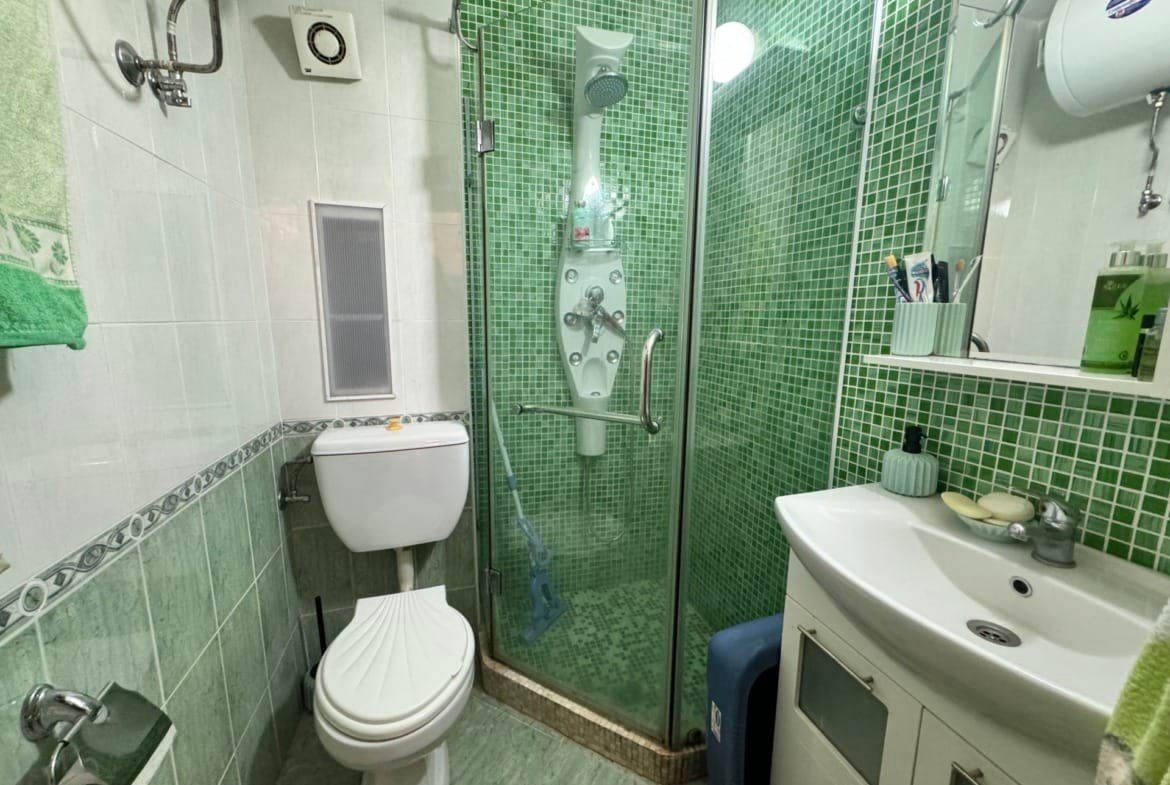 Современная ванная комната с душевой кабиной, унитазом и раковиной, оформленная в зелёных тонах. Идеально для жилья в Болгарии.